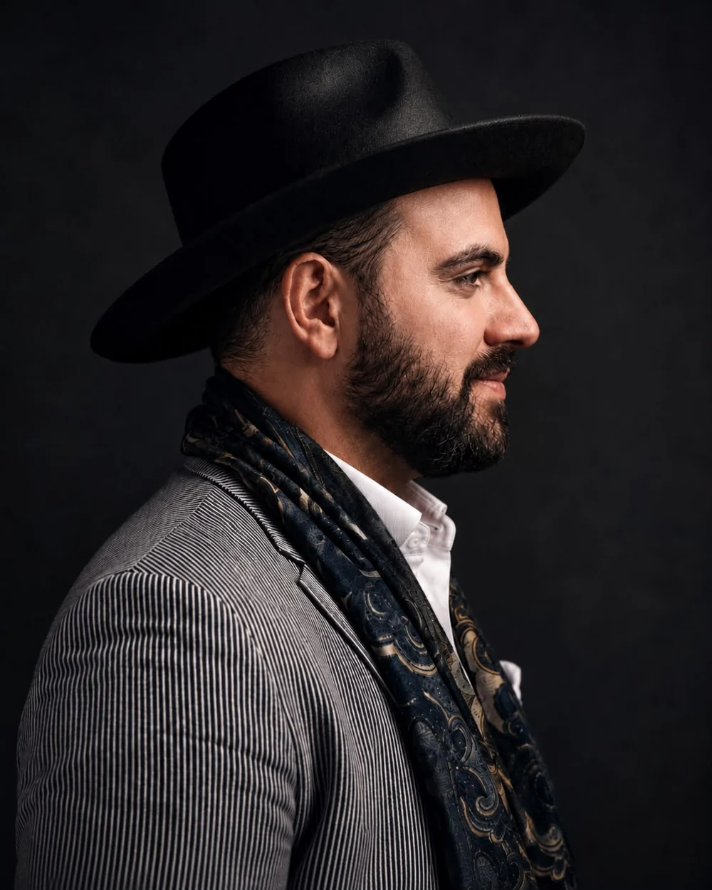 Andrea Zagatti, co-founder of Claves House, in profile wearing a dark fedora, patterned scarf and pinstripe jacket.